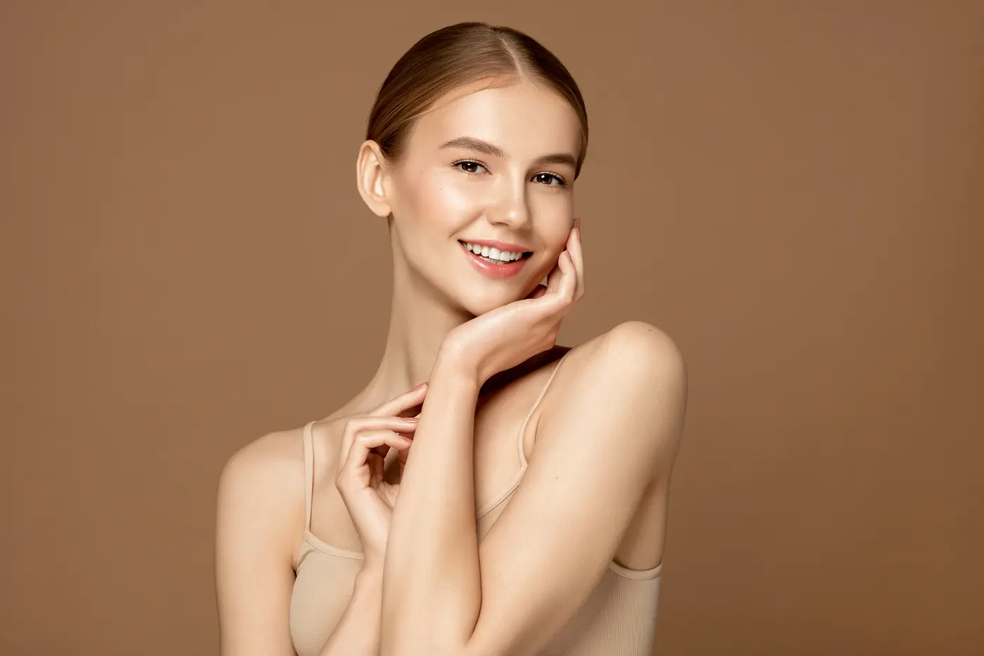 Smiling woman with clear skin and natural makeup touching face.